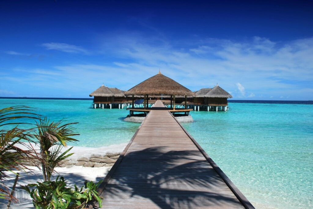 Wooden-pier-overwater-bungalow-thatched-roof-clear-blue-sea-bright-sky-scattered-clouds-turquoise-water-serene-vacation-spot