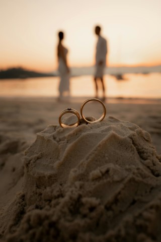 two-wedding-rings-on-sand-with-couple-background-at-sunset