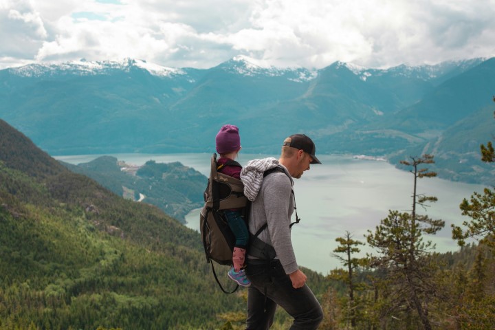 adult-carrying-child-in-backpack-overlooking-mountain-lake-scenery