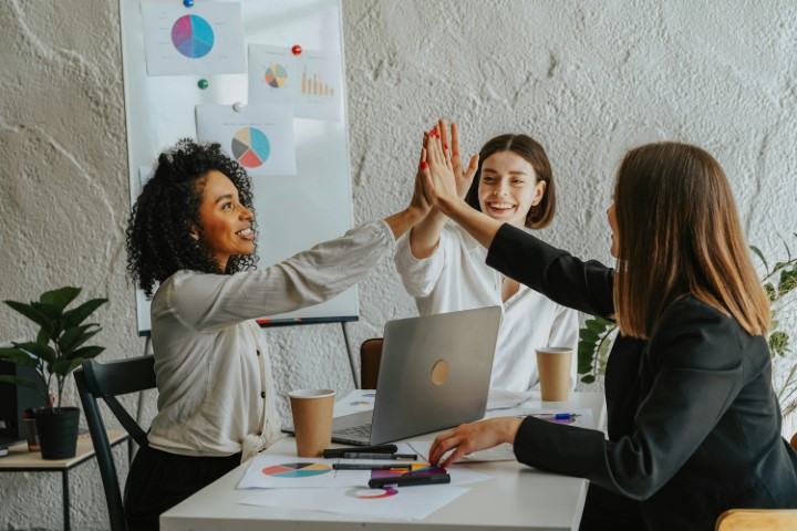 three-professionals-high-fiving-in-a-meeting-with-charts-in-background