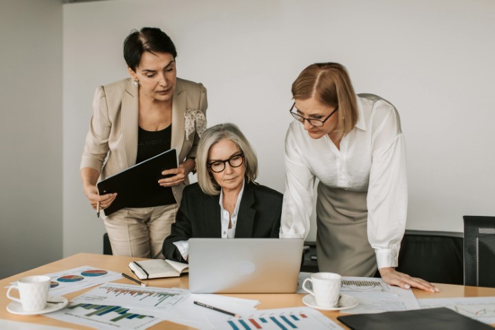 three-people-standing-around-laptop-with-papers-and-charts-faces-obscured